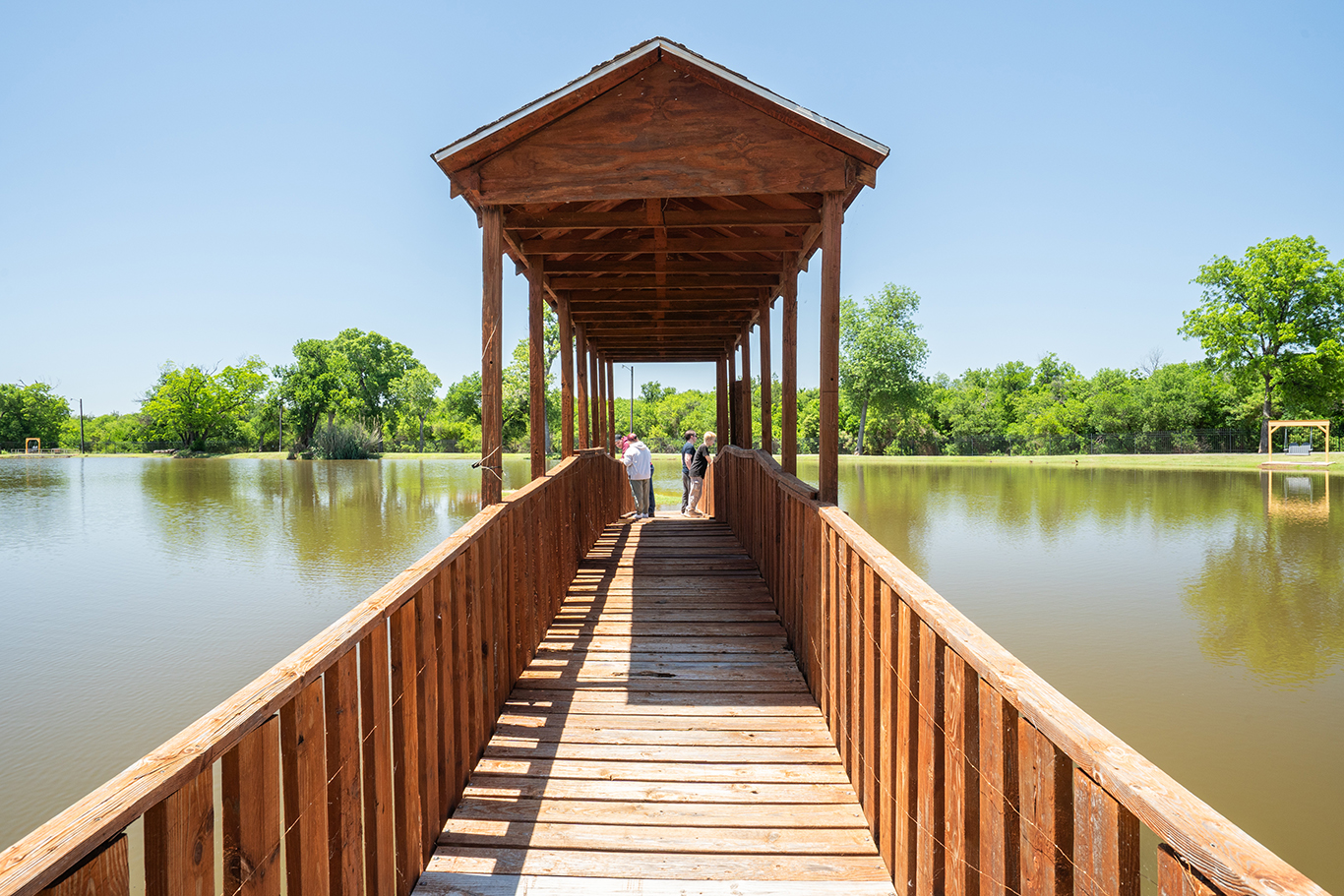 Covered wooden fishing pier overlooking scenic pond at Wichita Falls RV Park with peaceful waterfront recreation and shaded camping sites.